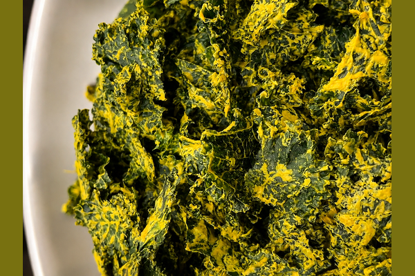 SpaJuiceBar cheesy kale chips in a tan bowl.  The chips are dehydrated with a sauce on top  