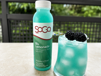 SOGO Blu Lemonade bottle next to a glass of blue lemonade with blackberries on top