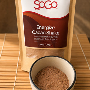 Energize Cacao Shake bag with a cup of the energize powder in front.  The items are on a straw mat