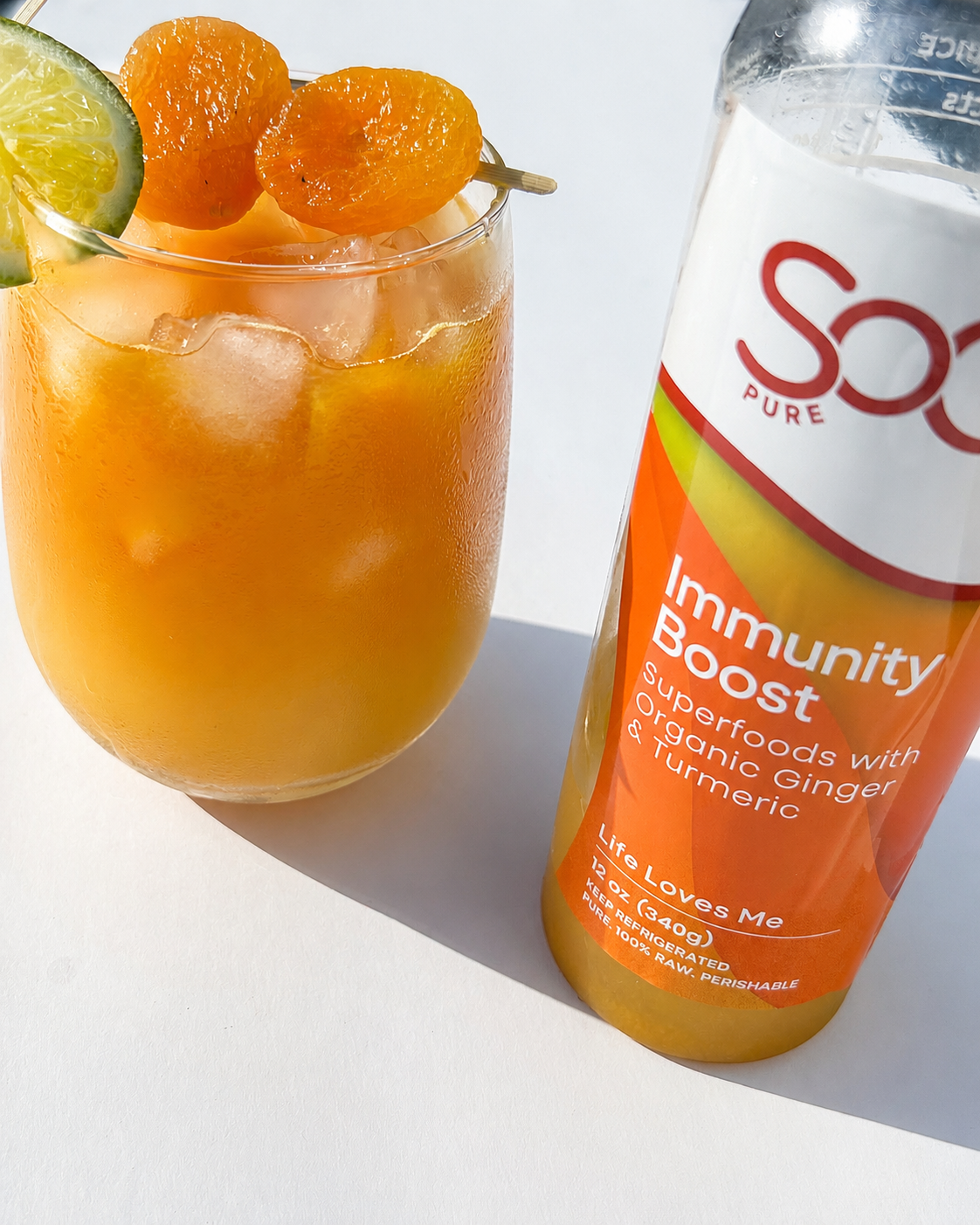 SoGo Pure Immunity Boost juice bottle beside the juice mocktail with lime and apricot garnish, with  ice on a bright white background.